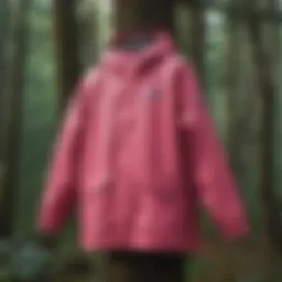 A vibrant pink Columbia rain jacket hanging on a tree branch in a forest.